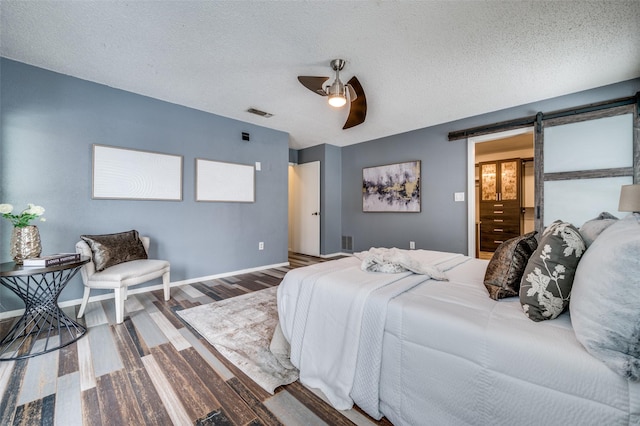 bedroom with a barn door, ceiling fan, a textured ceiling, and hardwood / wood-style flooring