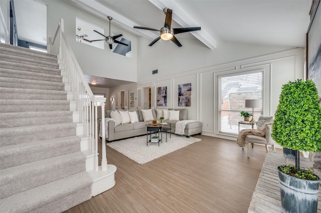 living room with beamed ceiling, ceiling fan, wood-type flooring, and a towering ceiling