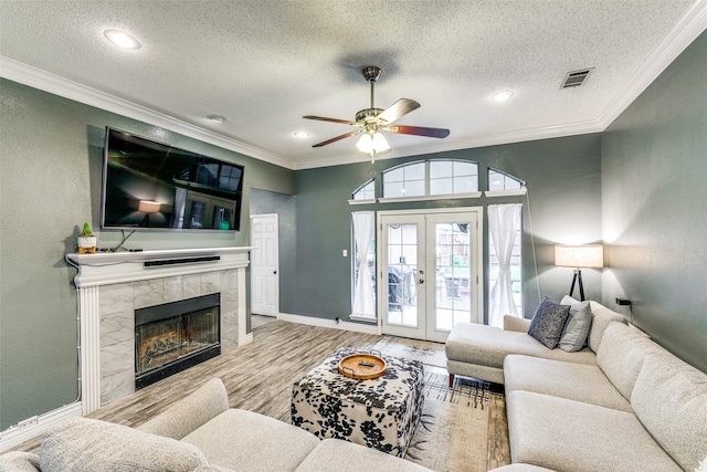 living room featuring french doors, hardwood / wood-style flooring, ceiling fan, a textured ceiling, and a tiled fireplace