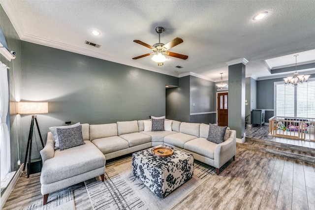 living room featuring wood-type flooring, a textured ceiling, a tray ceiling, ceiling fan with notable chandelier, and ornamental molding