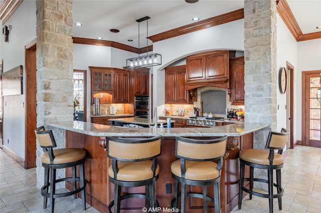 kitchen featuring kitchen peninsula, backsplash, light stone counters, and ornate columns