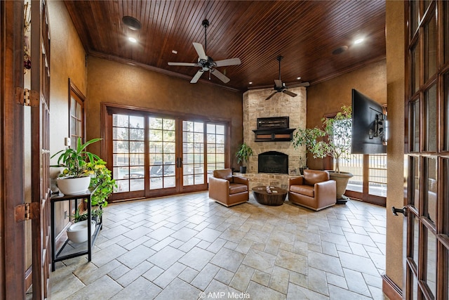 living room with ceiling fan, french doors, a high ceiling, a stone fireplace, and wood ceiling