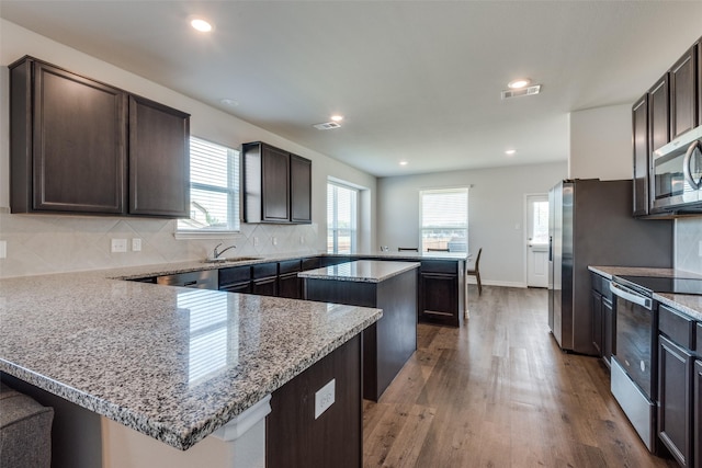 kitchen featuring light stone countertops, appliances with stainless steel finishes, kitchen peninsula, sink, and a kitchen island