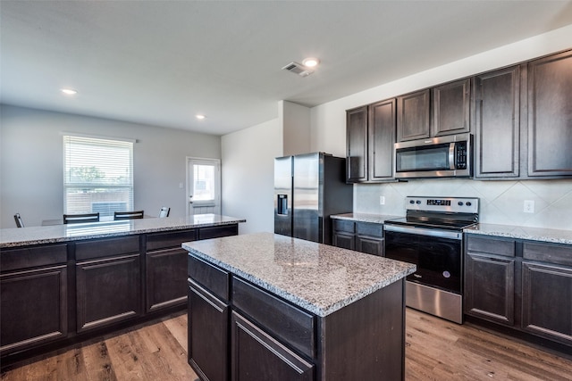 kitchen featuring dark brown cabinetry, hardwood / wood-style floors, decorative backsplash, a kitchen island, and appliances with stainless steel finishes