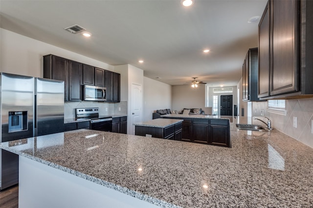 kitchen featuring a center island, sink, light stone countertops, appliances with stainless steel finishes, and kitchen peninsula