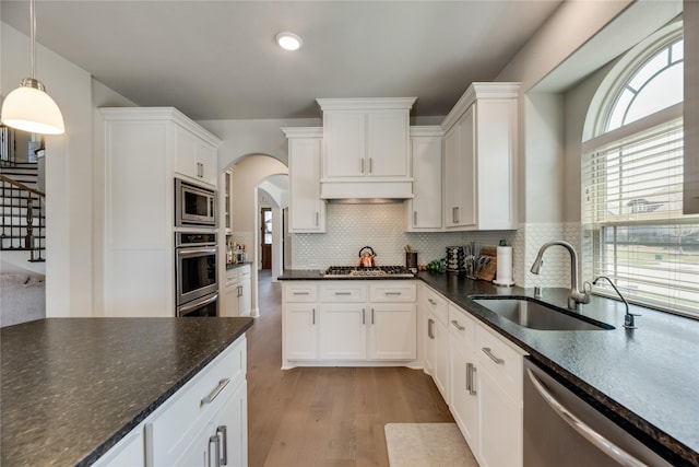 kitchen with appliances with stainless steel finishes, backsplash, sink, white cabinets, and hanging light fixtures