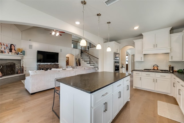 kitchen with lofted ceiling, hanging light fixtures, a kitchen island, white cabinetry, and stainless steel appliances