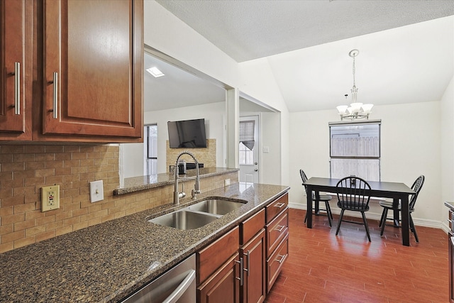 kitchen with dark stone counters, hanging light fixtures, sink, vaulted ceiling, and a notable chandelier