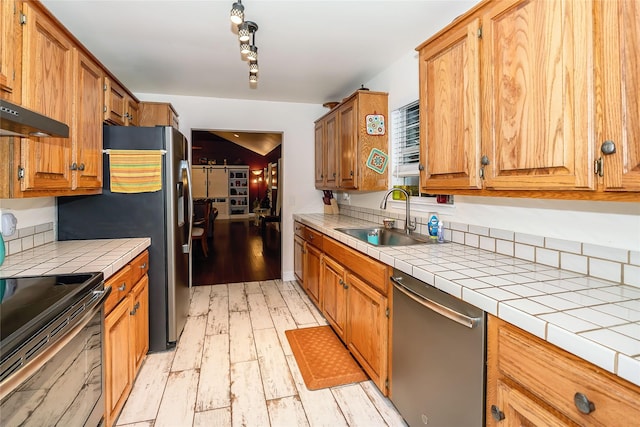 kitchen featuring tile countertops, track lighting, sink, light wood-type flooring, and appliances with stainless steel finishes