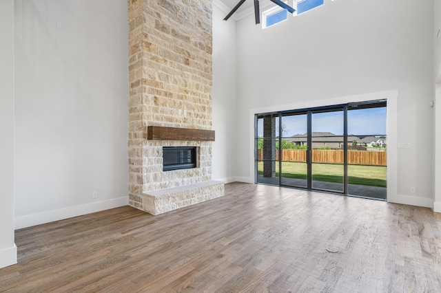 unfurnished living room featuring a stone fireplace, a towering ceiling, wood-type flooring, and a wealth of natural light