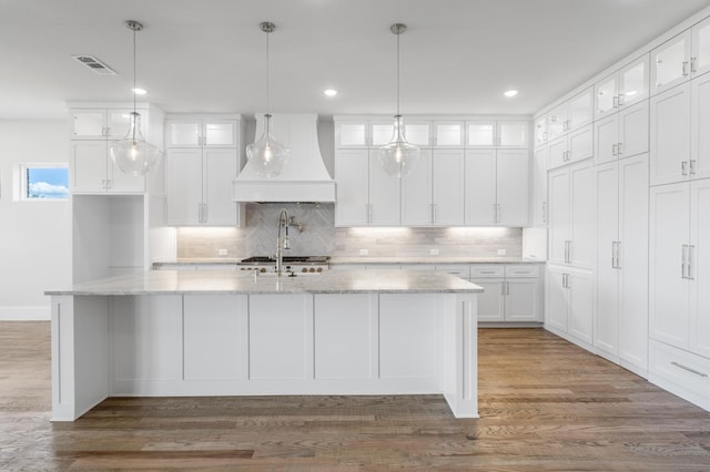 kitchen with white cabinetry, an island with sink, light stone counters, and custom exhaust hood