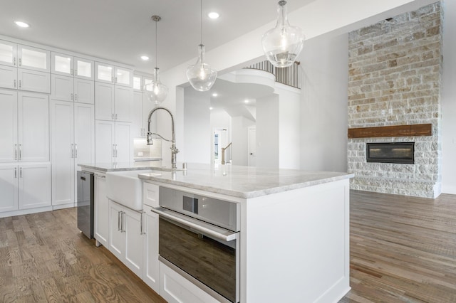 kitchen featuring pendant lighting, white cabinetry, oven, and a kitchen island with sink