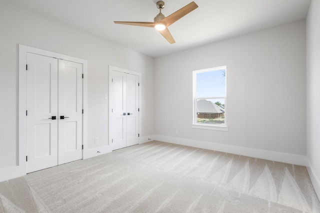 unfurnished bedroom featuring carpet floors, two closets, and ceiling fan