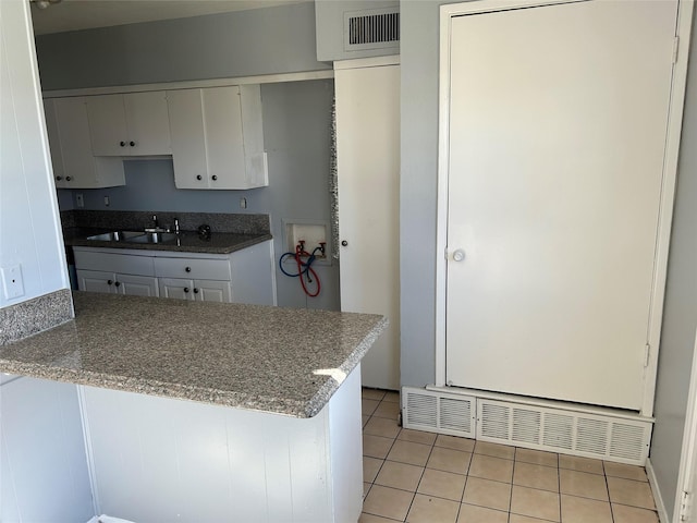 kitchen with kitchen peninsula, white cabinets, sink, and light tile patterned floors