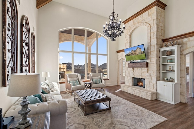 living room featuring a stone fireplace, a towering ceiling, dark wood-type flooring, and a chandelier