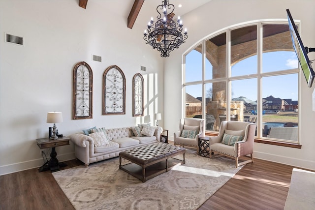 living room with beamed ceiling, a towering ceiling, hardwood / wood-style flooring, and an inviting chandelier