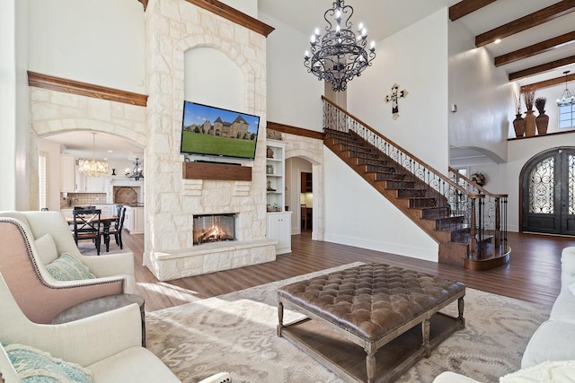 living room with a stone fireplace, a chandelier, wood-type flooring, and a high ceiling