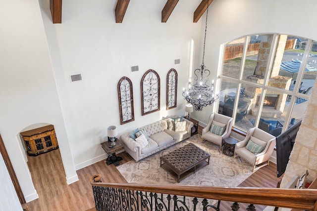 living room featuring a chandelier, beam ceiling, a high ceiling, and light hardwood / wood-style flooring