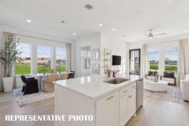 kitchen with white cabinets, light hardwood / wood-style floors, sink, ceiling fan, and a center island with sink