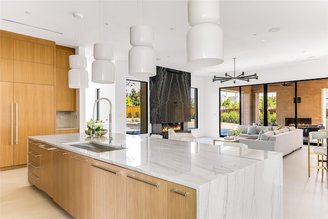 kitchen with a large island with sink, a large fireplace, hanging light fixtures, and sink