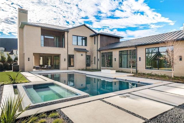 rear view of property with a patio area, a balcony, and a pool with hot tub