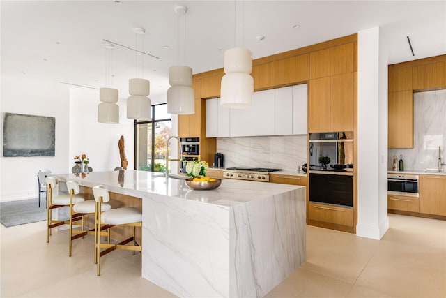 kitchen with decorative backsplash, stainless steel gas cooktop, hanging light fixtures, and a kitchen island with sink