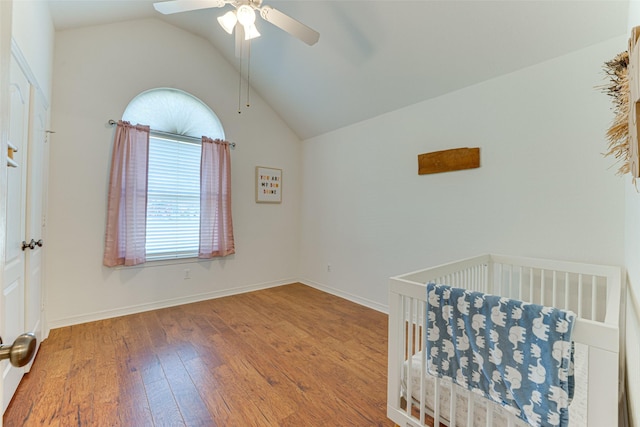 unfurnished bedroom featuring wood-type flooring, a nursery area, ceiling fan, and lofted ceiling