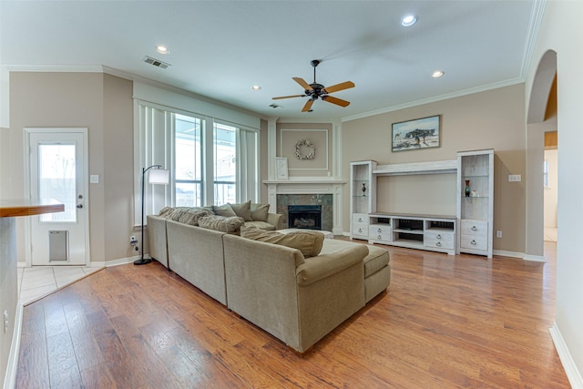 living room featuring a tile fireplace, light hardwood / wood-style floors, ceiling fan, and ornamental molding