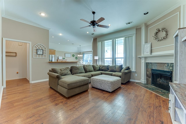 living room featuring hardwood / wood-style floors, ceiling fan, crown molding, and a tiled fireplace