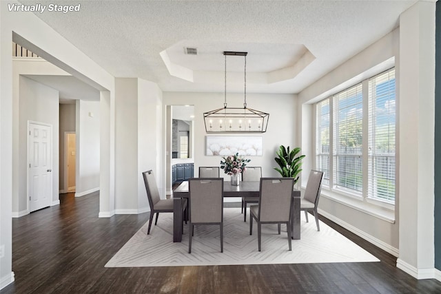 dining space with a textured ceiling, a raised ceiling, dark wood-type flooring, and a chandelier