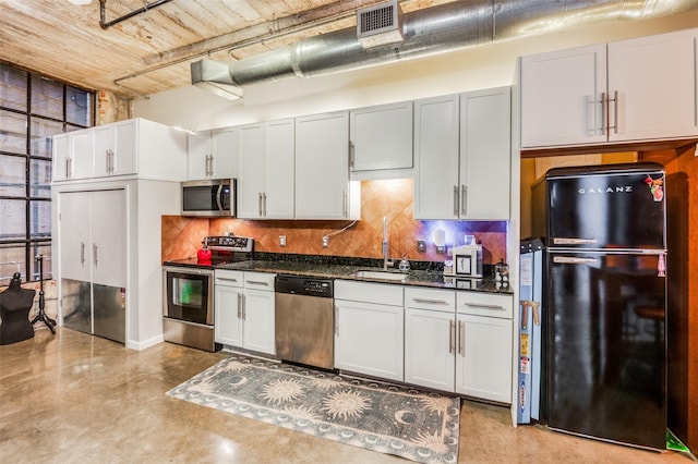 kitchen with tasteful backsplash, stainless steel appliances, sink, dark stone countertops, and white cabinetry