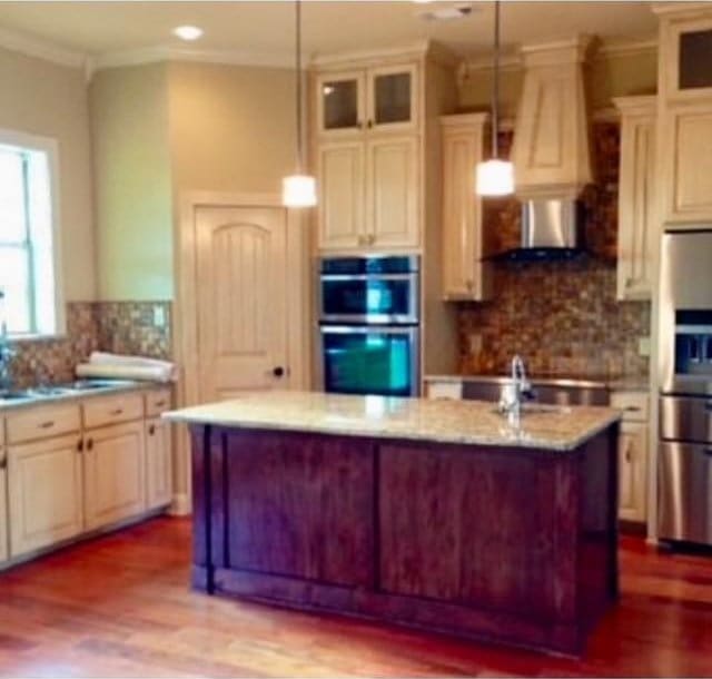 kitchen with light stone counters, wall chimney exhaust hood, backsplash, hanging light fixtures, and appliances with stainless steel finishes