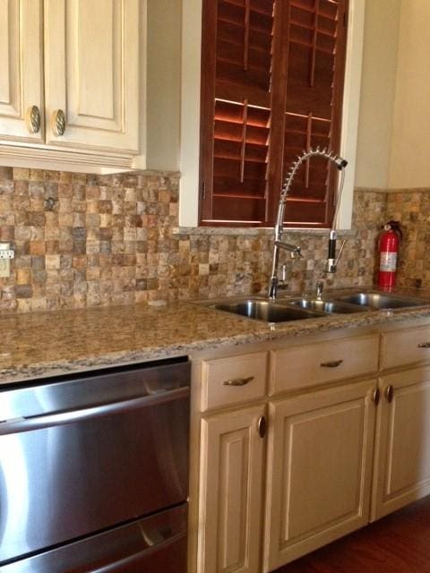 kitchen with light stone counters, dishwasher, backsplash, and sink