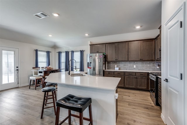 kitchen with a kitchen bar, stainless steel appliances, sink, a center island with sink, and light hardwood / wood-style floors