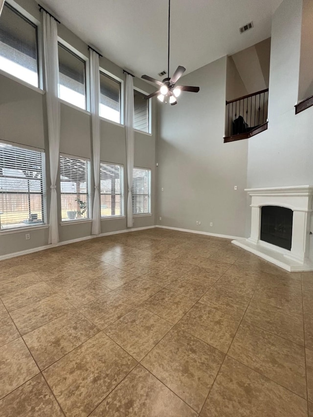 unfurnished living room featuring visible vents, a fireplace with raised hearth, a towering ceiling, a ceiling fan, and baseboards