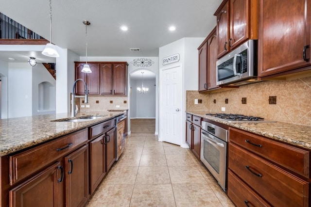 kitchen featuring arched walkways, stainless steel appliances, a sink, and light stone countertops