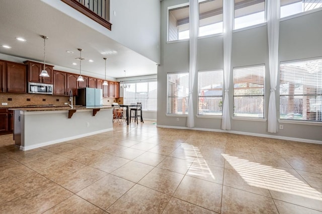 kitchen with light tile patterned floors, a kitchen island with sink, baseboards, freestanding refrigerator, and stainless steel microwave