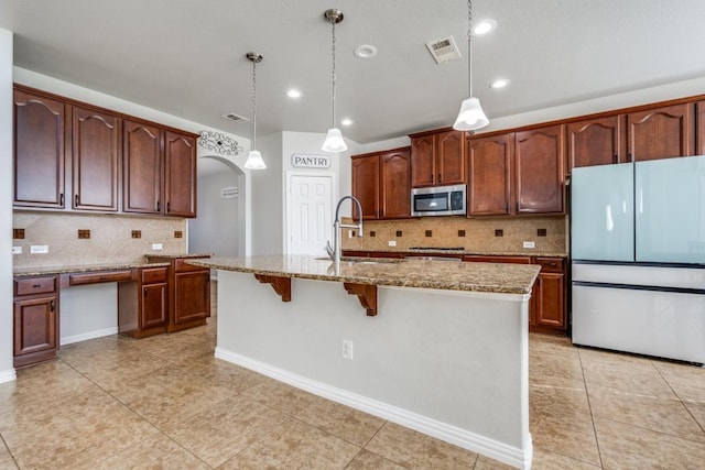 kitchen featuring arched walkways, light stone counters, stainless steel microwave, freestanding refrigerator, and a sink