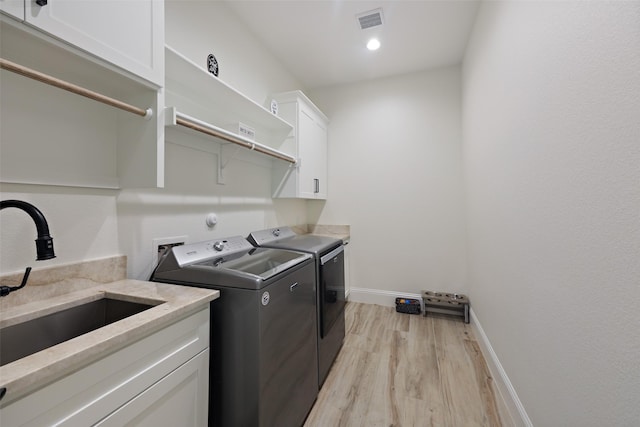 laundry room featuring washer and clothes dryer, cabinets, light wood-type flooring, and sink