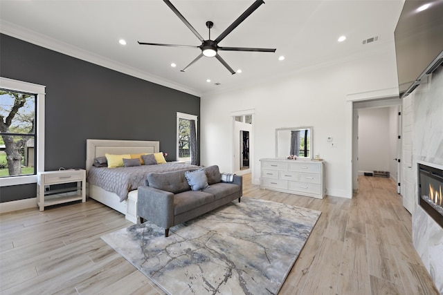 bedroom with a tiled fireplace, ceiling fan, light hardwood / wood-style flooring, and multiple windows