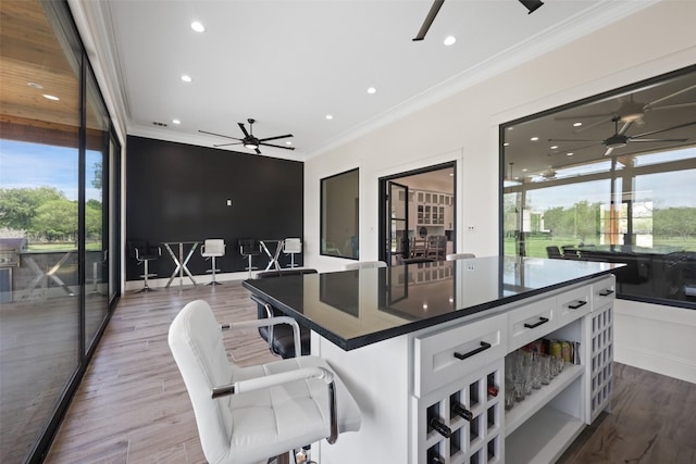 kitchen featuring a kitchen island, wood-type flooring, a kitchen bar, white cabinets, and ornamental molding