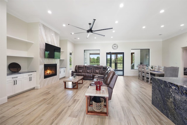 living room with light wood-type flooring, built in features, crown molding, and a premium fireplace