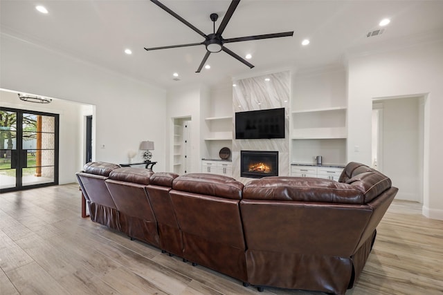 living room with a high end fireplace, crown molding, ceiling fan, light wood-type flooring, and built in features