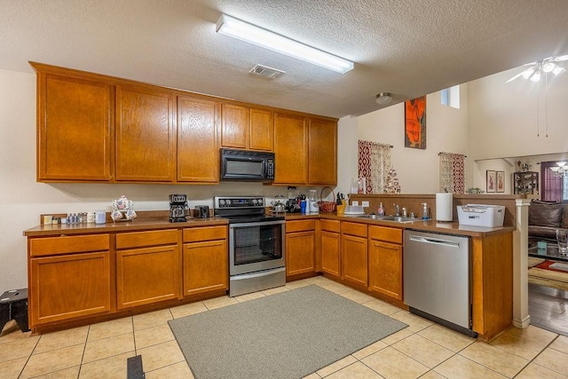 kitchen with appliances with stainless steel finishes, kitchen peninsula, light tile patterned floors, a textured ceiling, and sink