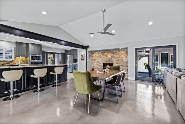 dining space featuring vaulted ceiling, a stone fireplace, ceiling fan, and sink