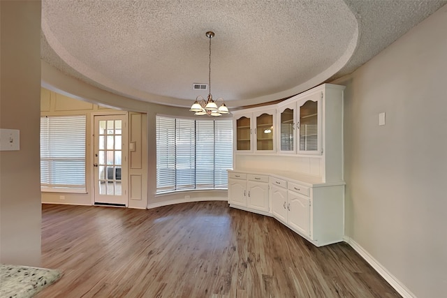 unfurnished dining area with light wood-type flooring, a textured ceiling, and an inviting chandelier