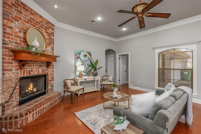 living room featuring hardwood / wood-style flooring, ceiling fan, a fireplace, and crown molding