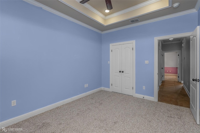 unfurnished bedroom with ceiling fan, a raised ceiling, crown molding, light carpet, and a closet