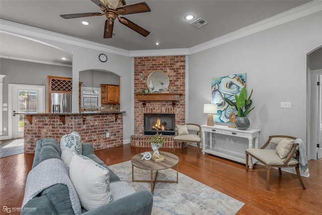 living room featuring light wood-type flooring, a brick fireplace, ceiling fan, and ornamental molding