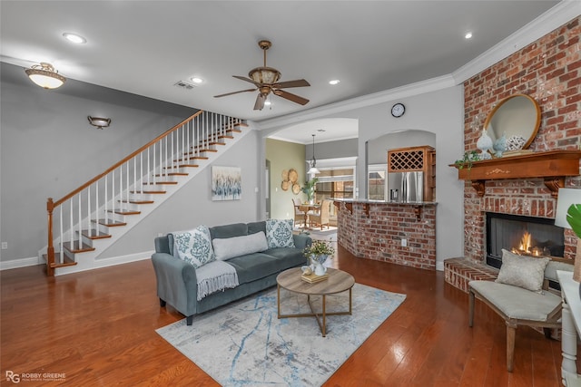 living room with ceiling fan, ornamental molding, dark wood-type flooring, and a brick fireplace